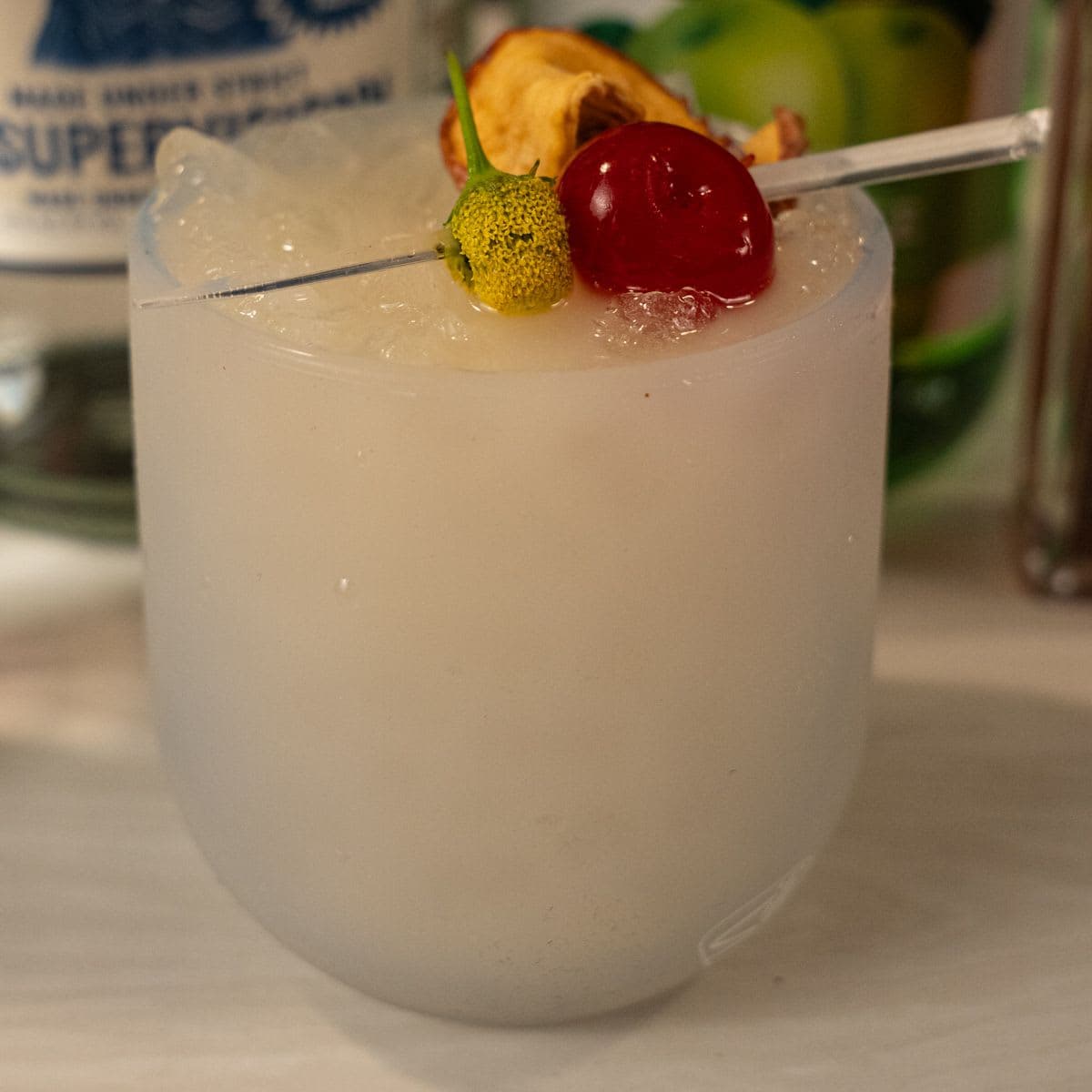 Happle Juice copycat cocktail in a Silipint cup with buzz button, cherry, and dried apple garnish